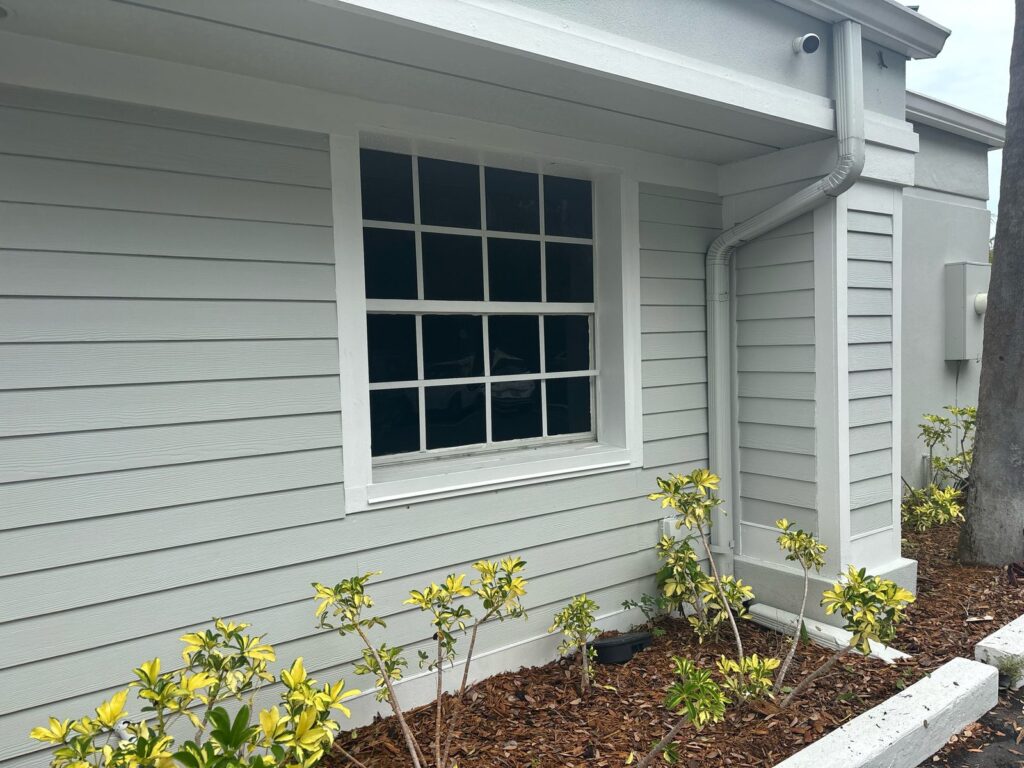 Gray commercial siding with a white-trimmed window, column, and downspout