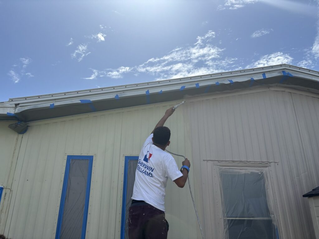 Purple Painting painter rolling an exterior wall with windows masked for protection